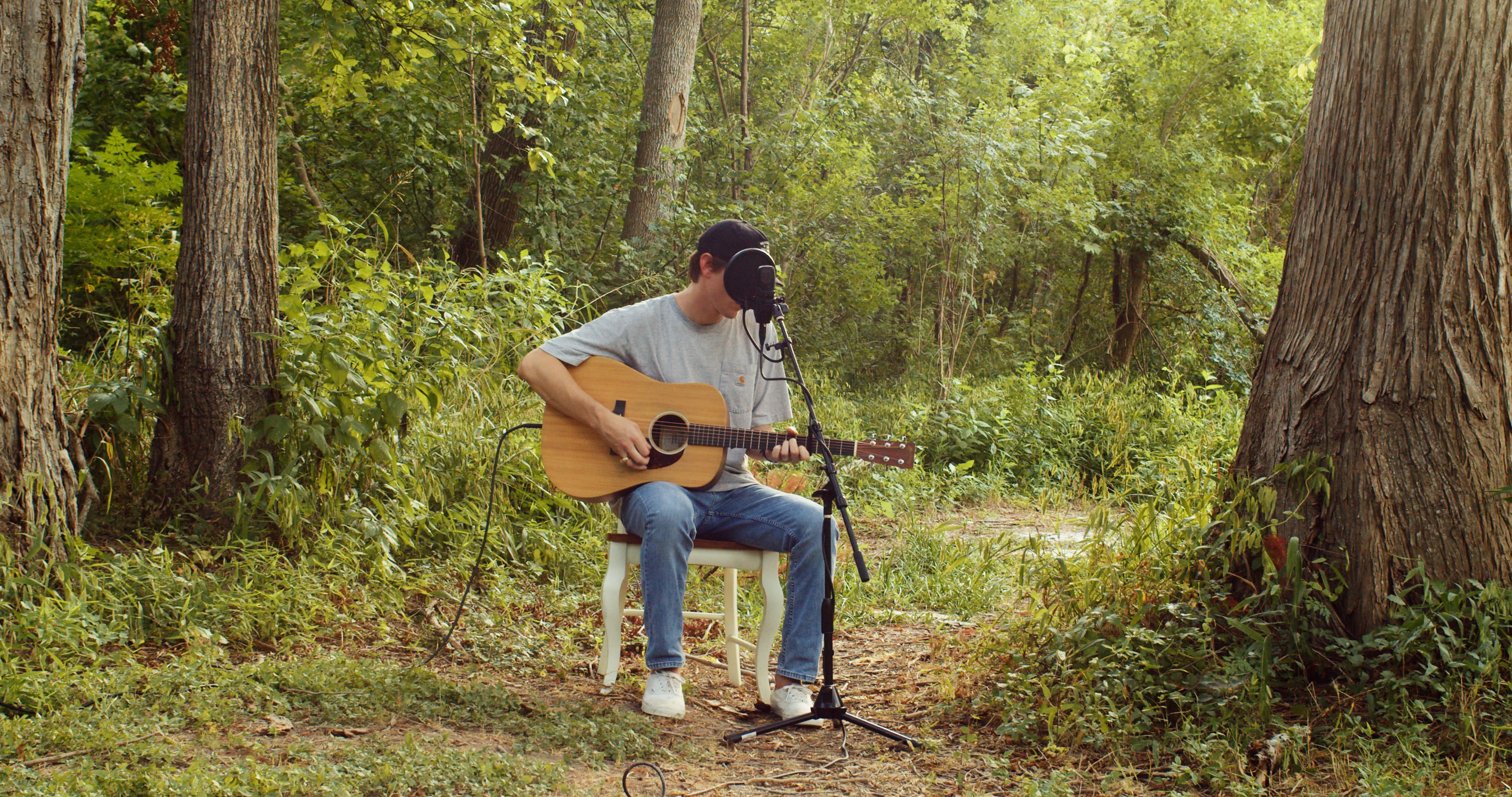 Wide shot of Dylan Gossett playing guitar in the woods